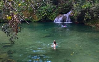 Blonde woman swimming in a natural swimming hole with a waterfall