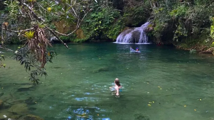 Blonde woman swimming in a natural swimming hole with a waterfall