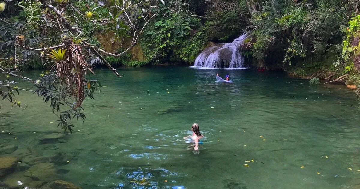 Blonde woman swimming in a natural swimming hole with a waterfall