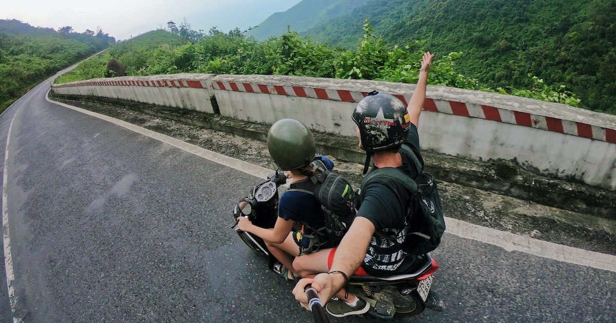 Two bikers riding down a road surrounded by jungle