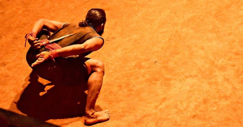 Crouched man clutching a sword behind his back