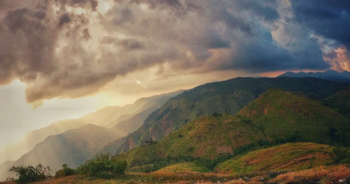 The sun rises over green slopes in a valley in Parunthumpara.