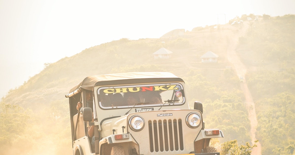 A grey jeep climbs an uphill slope surrounded by misty peaks in Ramakkalmedu.