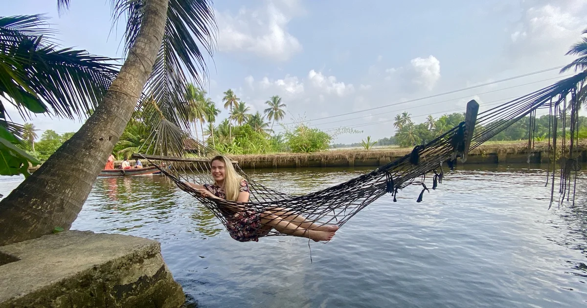 Author Escape Artist Katie wearing a dress in a string hammock over Alleppey backwaters