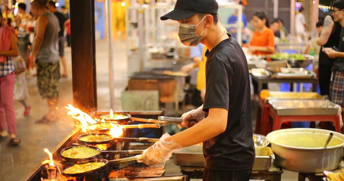 A man multi-tasks with three pans over a fire at the Da Nang night market.