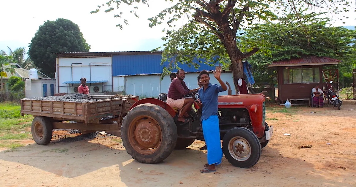 Two farmers waving alongside a red truck in the Cumbum Valley.