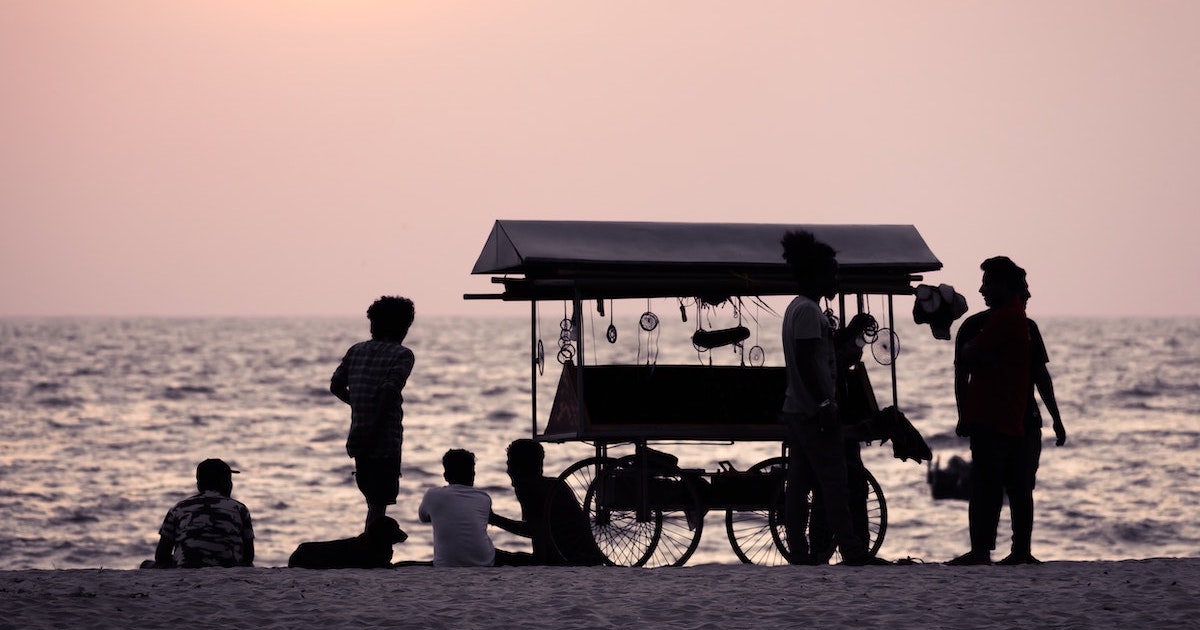 The shadow of a wagon and locals on Alleppey beach at sunset.