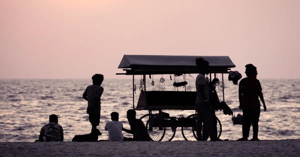 The shadow of a wagon and locals on Alleppey beach at sunset.