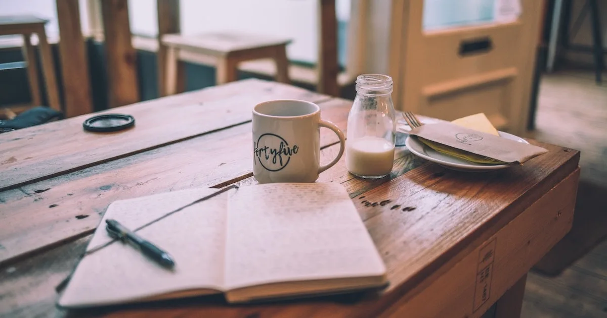 Travel journal laid out on a coffee shop table with a mug and glass of milk