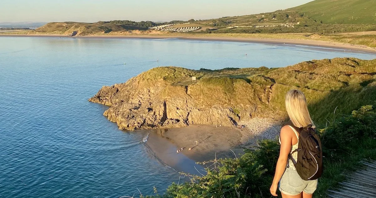Blonde girl looks out over a small cove called Broughton Corner in the Gower.