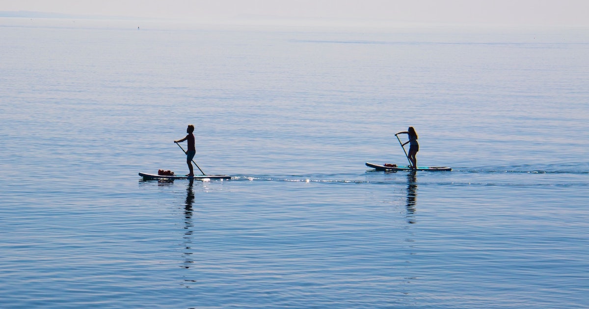 Two people paddleboard on calm ocean water in the Gower.