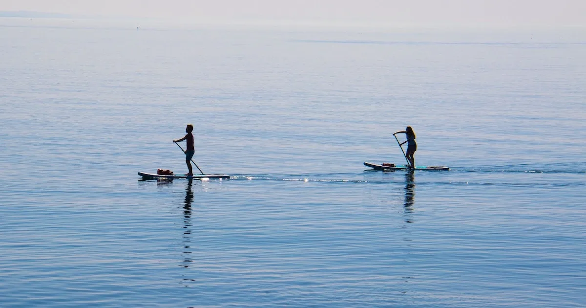 Two people paddleboard on calm ocean water in the Gower.