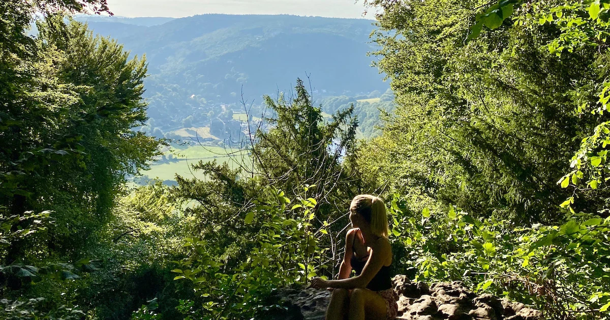 Blonde girl sits on the rock at the Devil's Pulpit viewpoint in the Wye Valley.