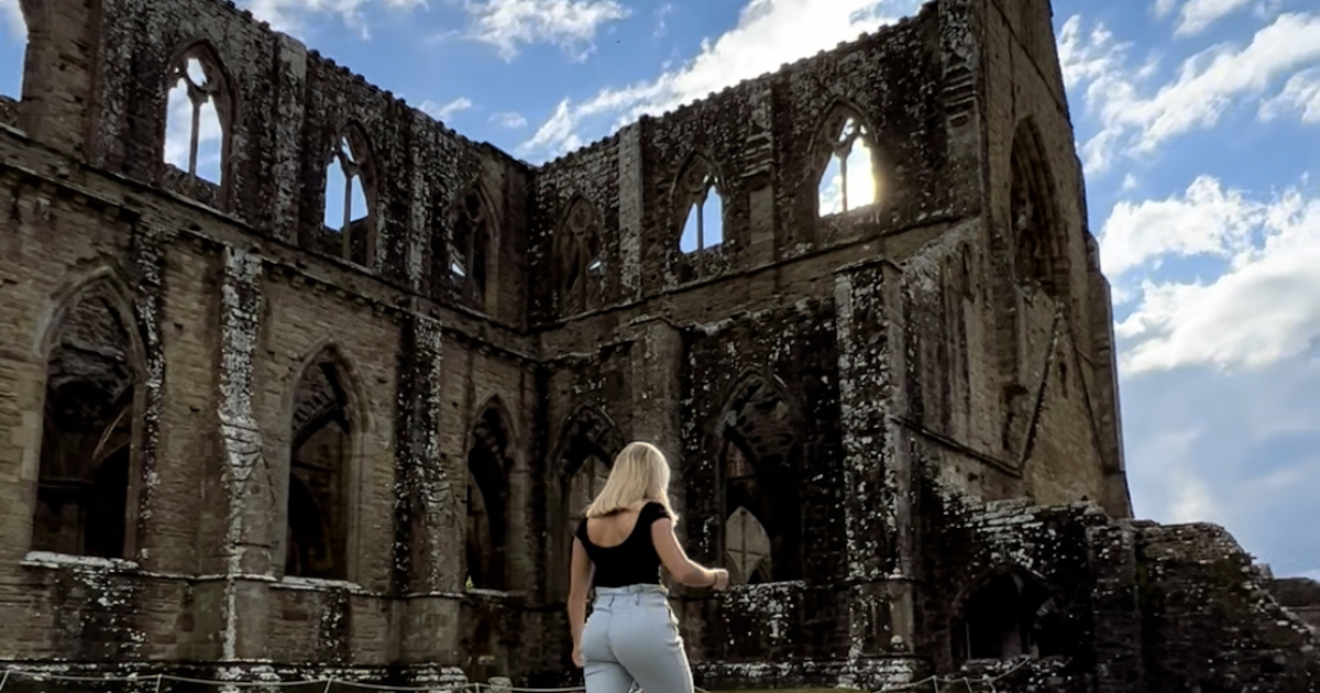 Girl walks in front of the Gothic Tintern Abbey.