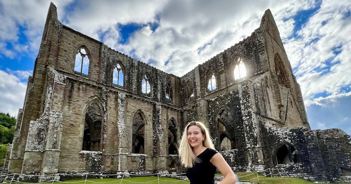 Blonde woman smiles at the camera in front of Tintern Abbey.