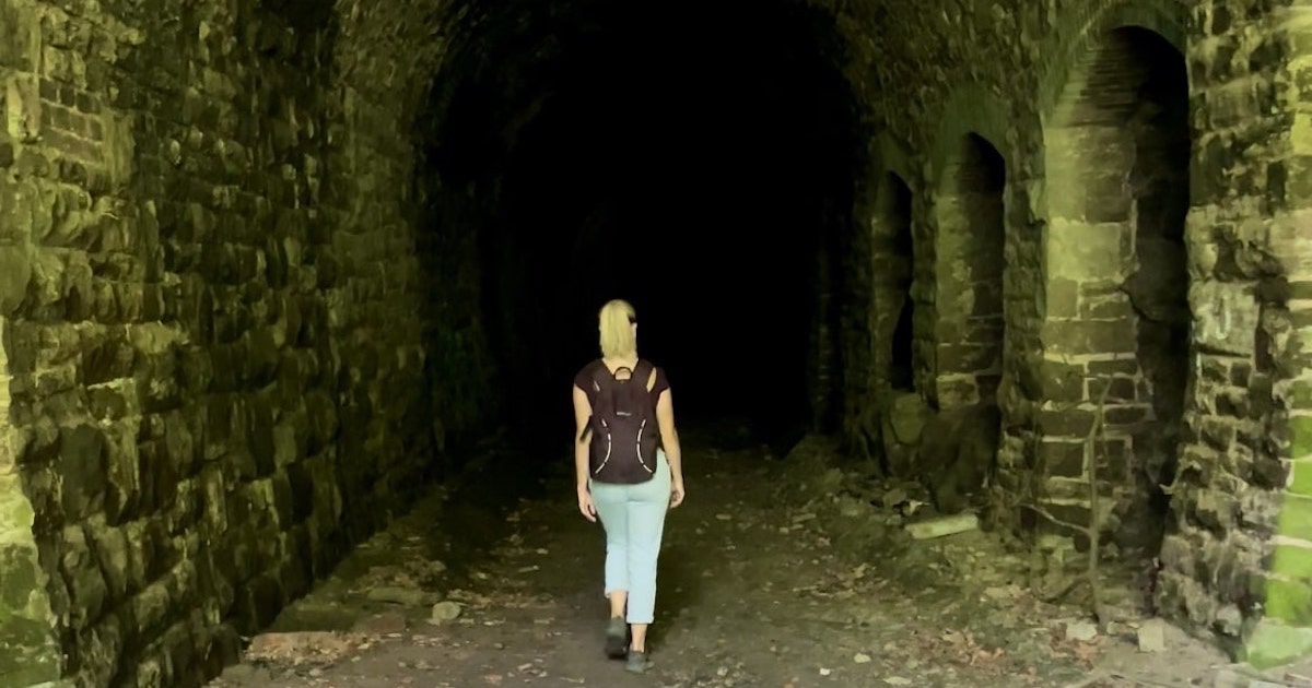 Blonde girl with a rucksack walks into the darkness of the Tiddenham Tunnel.