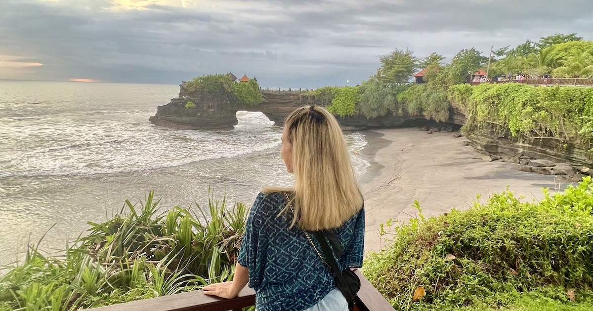 Blonde woman gazes out over the beach and Batu Bolong Temple from the surrounding cliffs.