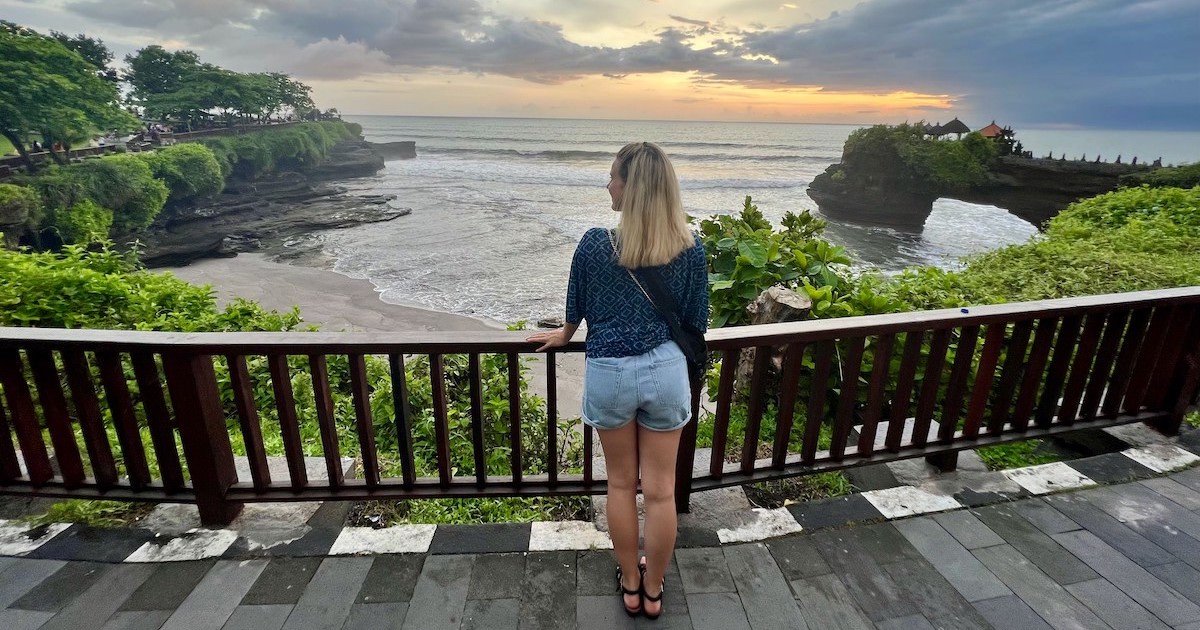 Blonde girl leans against the railing over Batu Bolong beach at sunset.