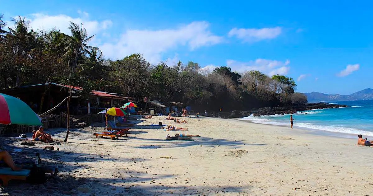 White sand backed by palm trees and Balinese warungs with umbrellas