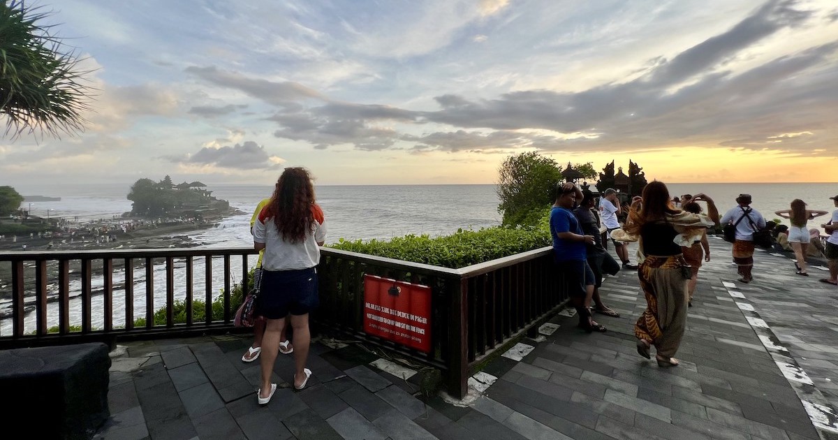 Tourists lean against the railings on the clifftop over Tanah Lot Temple.