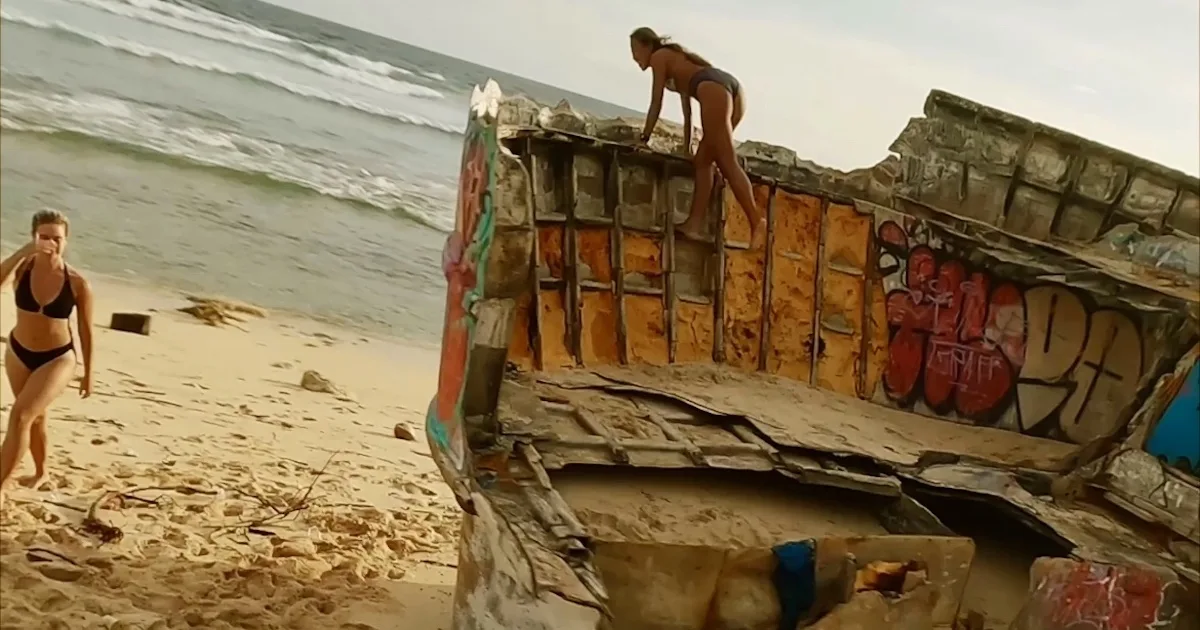 Two girls climb over the pink shipwreck on Nunggalan Beach.