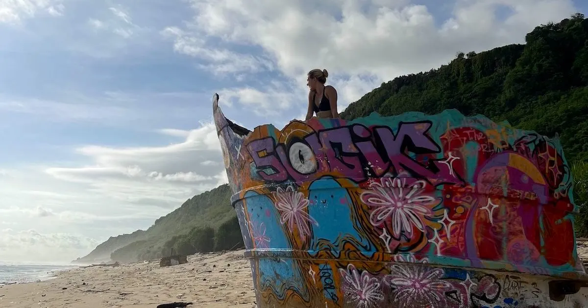 Blonde girl looks over Nunggalan Beach from a graffitied shipwreck.
