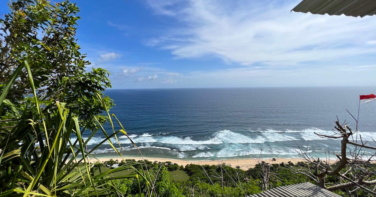 Views of blue waves crashing on golden sand from a warung above Nunggalan Beach.