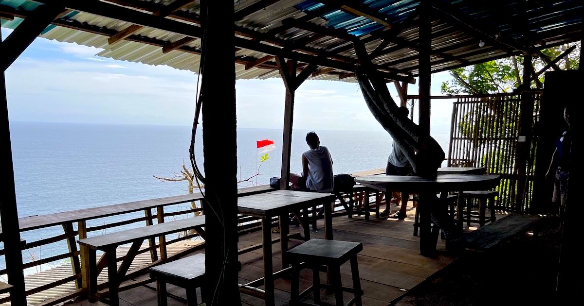 A clifftop warung with wooden seating and a sea view above Pantai Nunggalan.