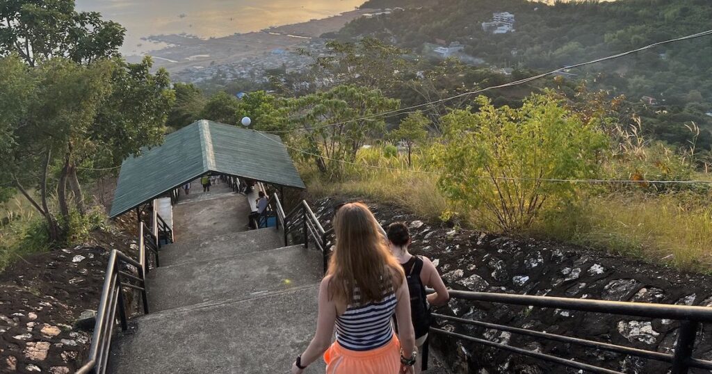 Brunette woman wearing neon orange shorts and a dark crop top walks down Mount Tapayas in Coron.