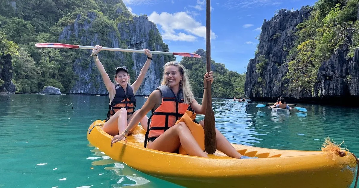 Two girls wear life jackets and bikinis in a kayak in Big Lagoon in El Nido.