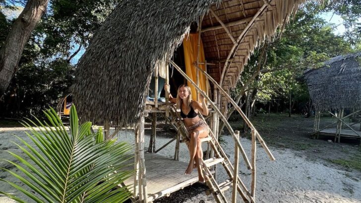 Girl sitting in a bamboo hut wears flowery cotton shorts and a halterneck bikini top.