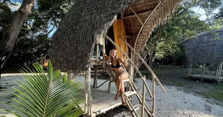 Girl sitting in a bamboo hut wears flowery cotton shorts and a halterneck bikini top.