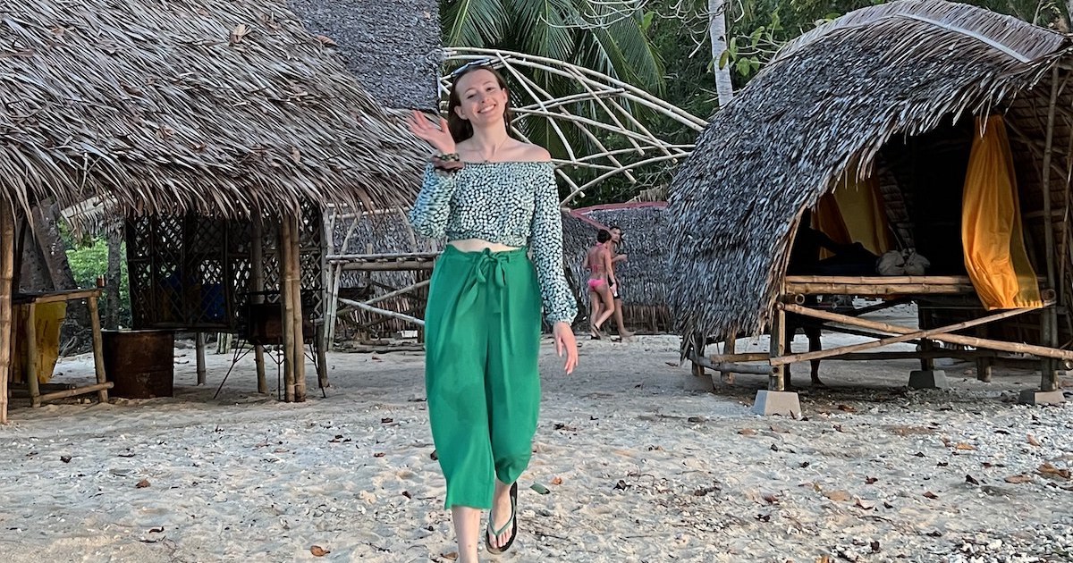 Girl wearing loose green trousers and a bardot crop top waves at the camera in Linacapan.