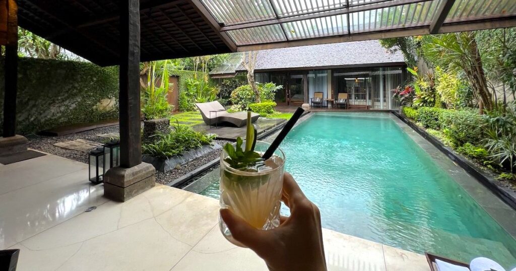 Hand holding a cocktail over the pool at luxury lifestyle Ametis Villa in Canggu.