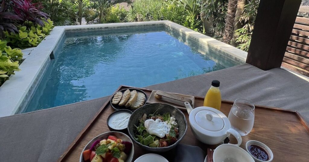A breakfast tray with juice, salad, and gluten-free bread in a villa in The Ungasan Clifftop Hotel.
