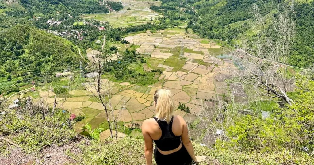 Woman wearing a sports crop top with bare shoulders sits on a hill overlooking the rice terrace basin in Harau Valley.