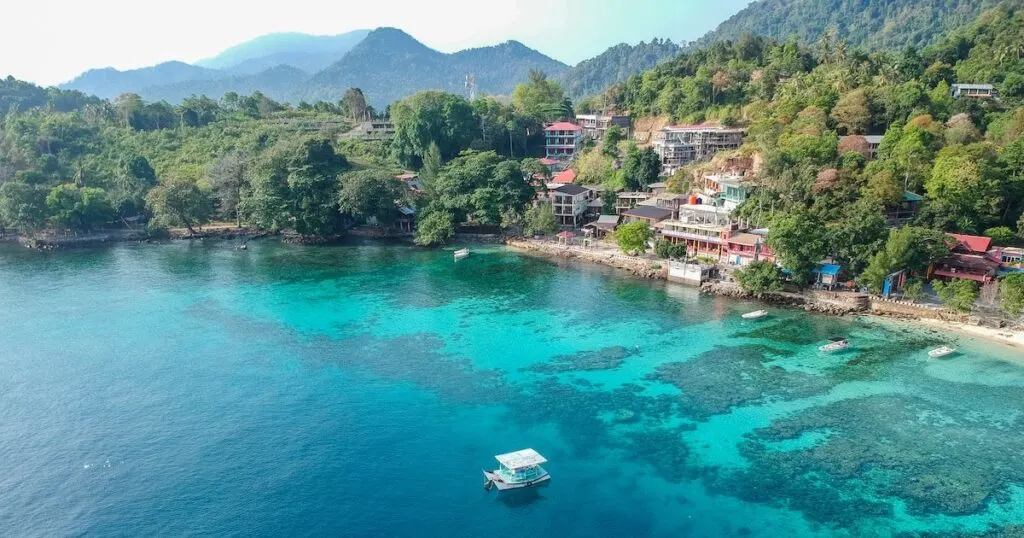 A boat floats in front of a remote beach with clear water and coral reefs in Sabang, West Sumatra.