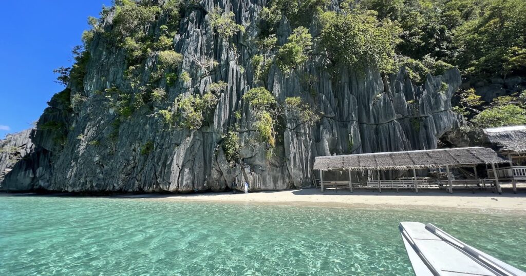 Shallow water next to limestone cliffs and a beach hut on Banul Beach in Coron.