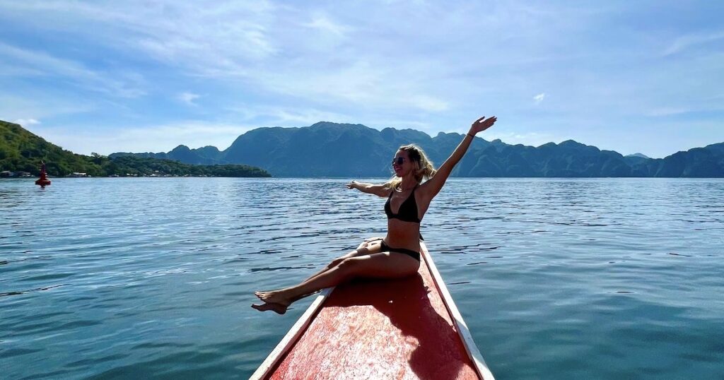 Girl wearing a bikini sits on the edge of a bangka boat while island hopping in Coron.
