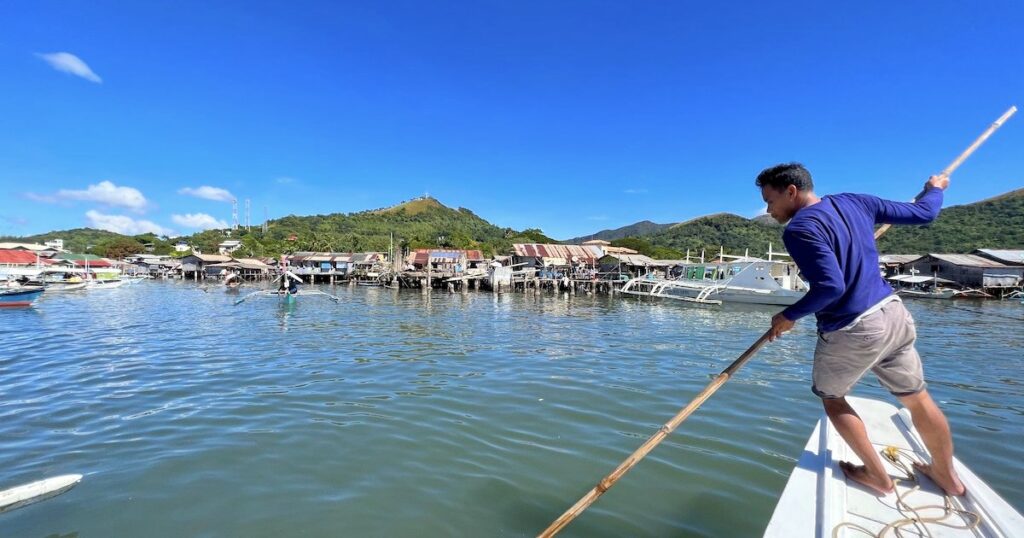 Coron tour guide uses a wooden pole to guide a bangka boat in Coron port.