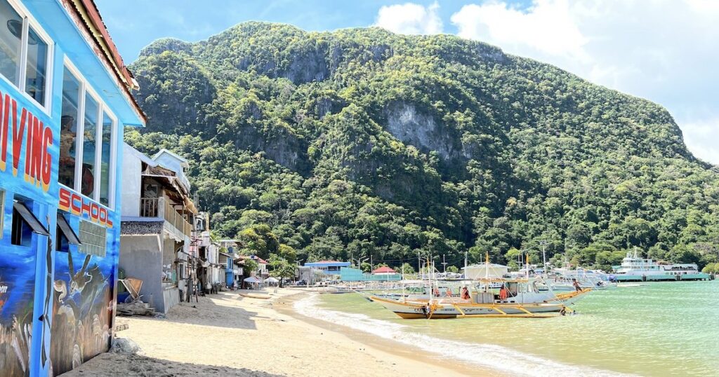 El Nido Beach lined with diving schools and bangka boats next to limestone cliffs.