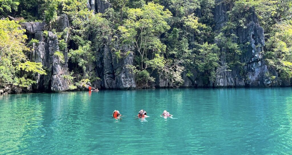 People wearing life jackets float in the clear waters of Kayangan Lake.