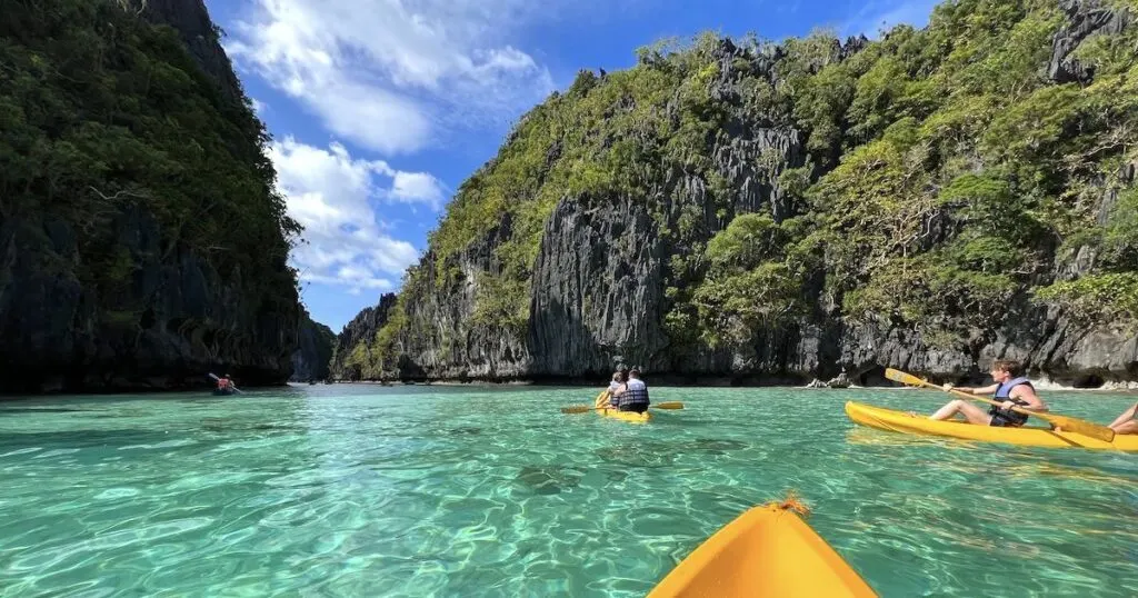 Kayakers on turquoise water on Big Lagoon in El Nido, surrounded by limestone cliffs.