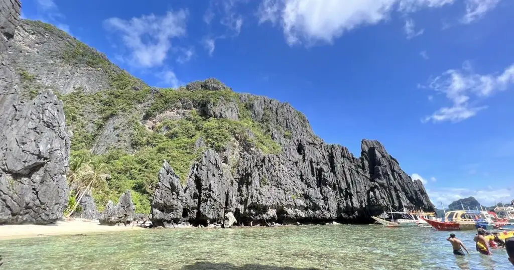 Jagged limestone rocks next to a white-sand beach on Shimizu Island in El Nido.