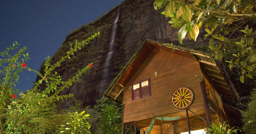 Starry skies over a wooden cabin and tall waterfall at Abdi Homestay.
