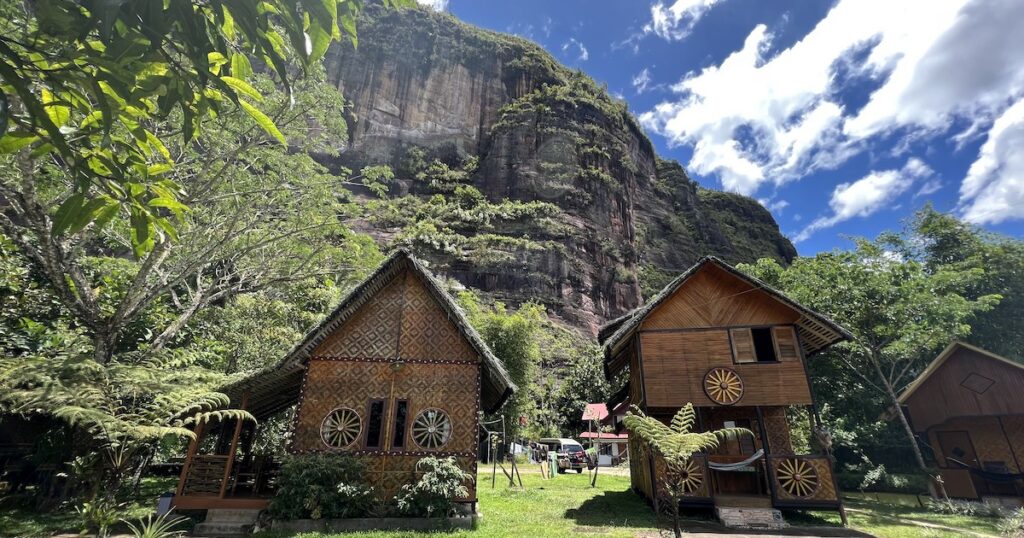 Wooden huts backed by sandstone cliffs at Abdi Homestay.