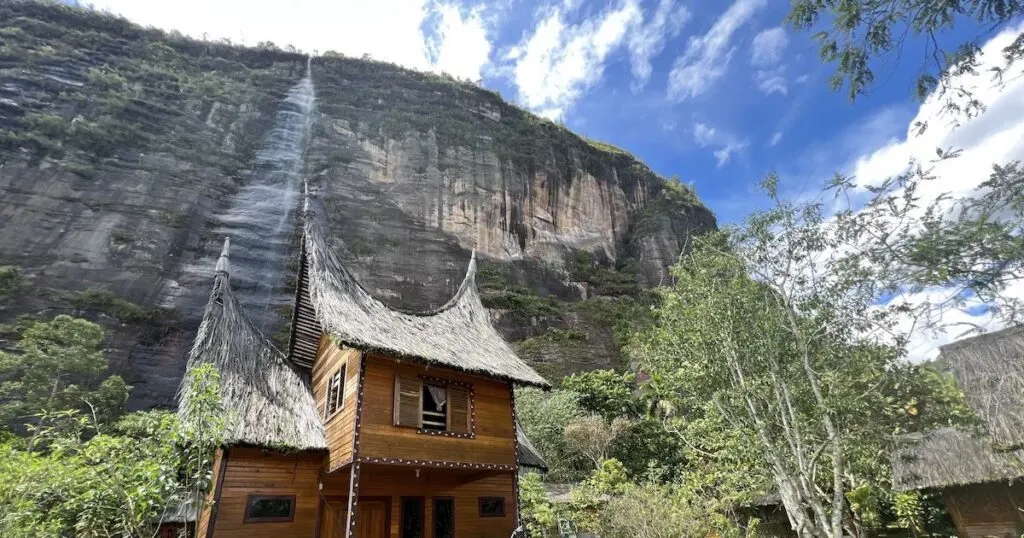 Minangkabau-style lodges at Abdi Homestay in Harau Valley, with a cliff and waterfall in the background.