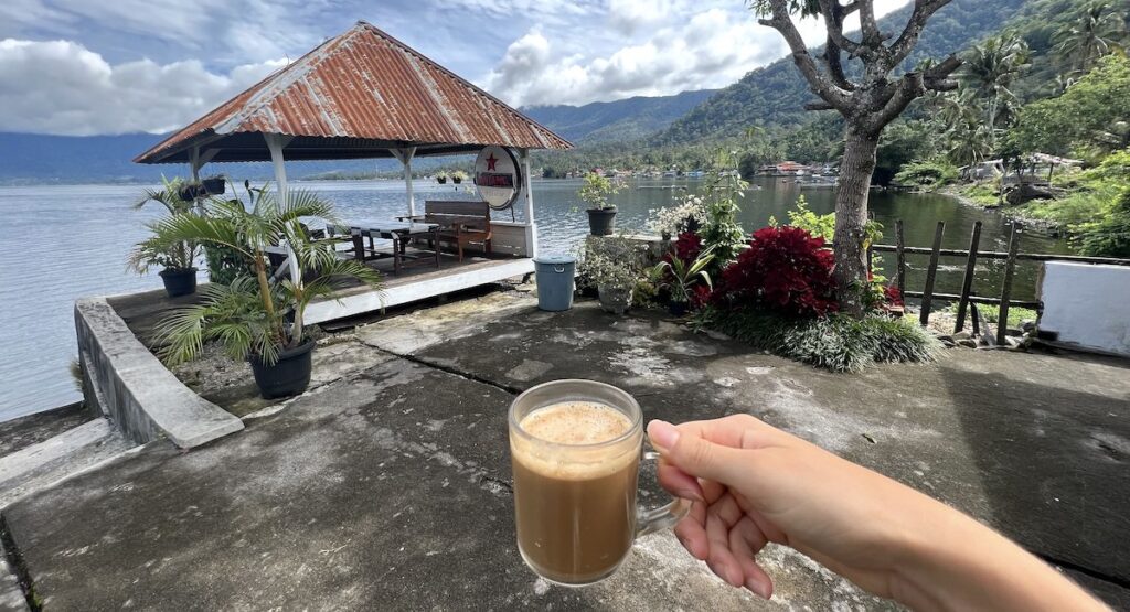 Hand holding a coffee at Beach Guesthouse overlooking Lake Maninjau.