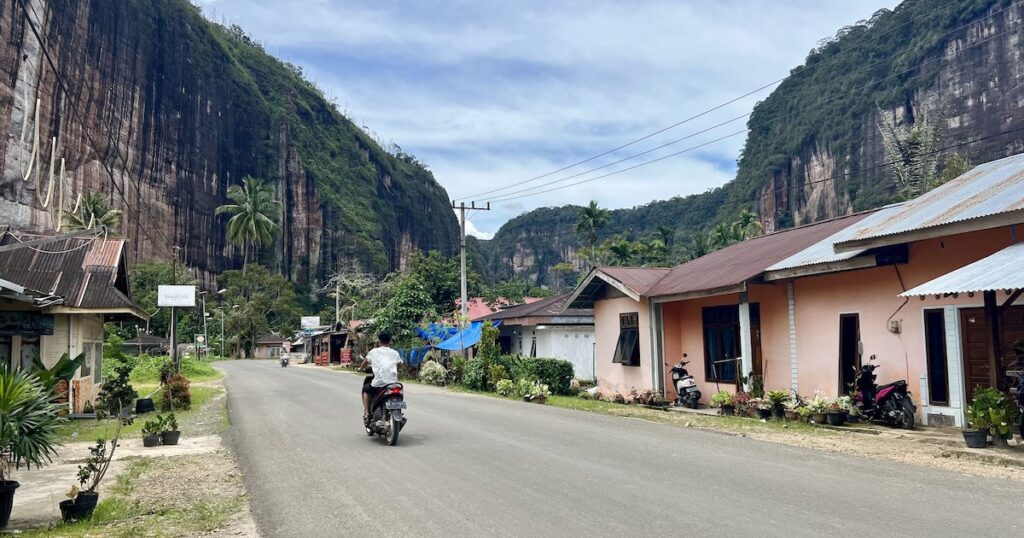 A scooter rider drives through the main street in Harau Valley.