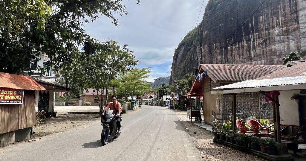 Man riding a scooter rides down a road with small houses in Harau.